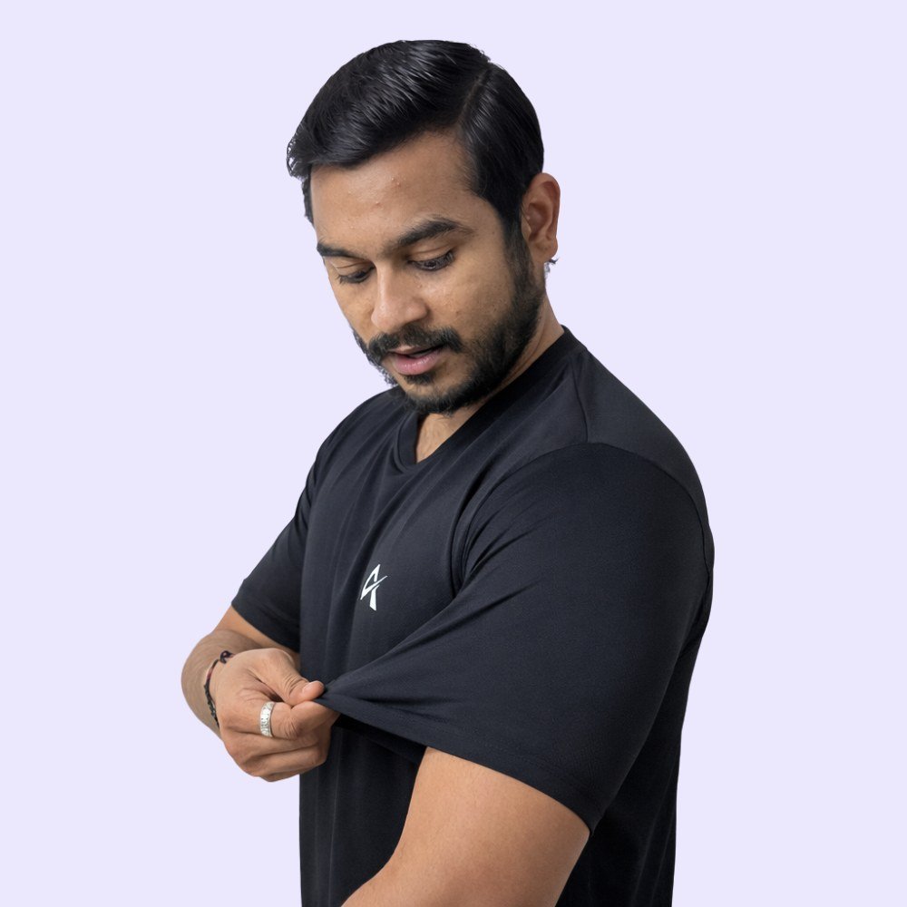 A man in a black shirt is showing strech of his t-shirt while standing in a neutral background.