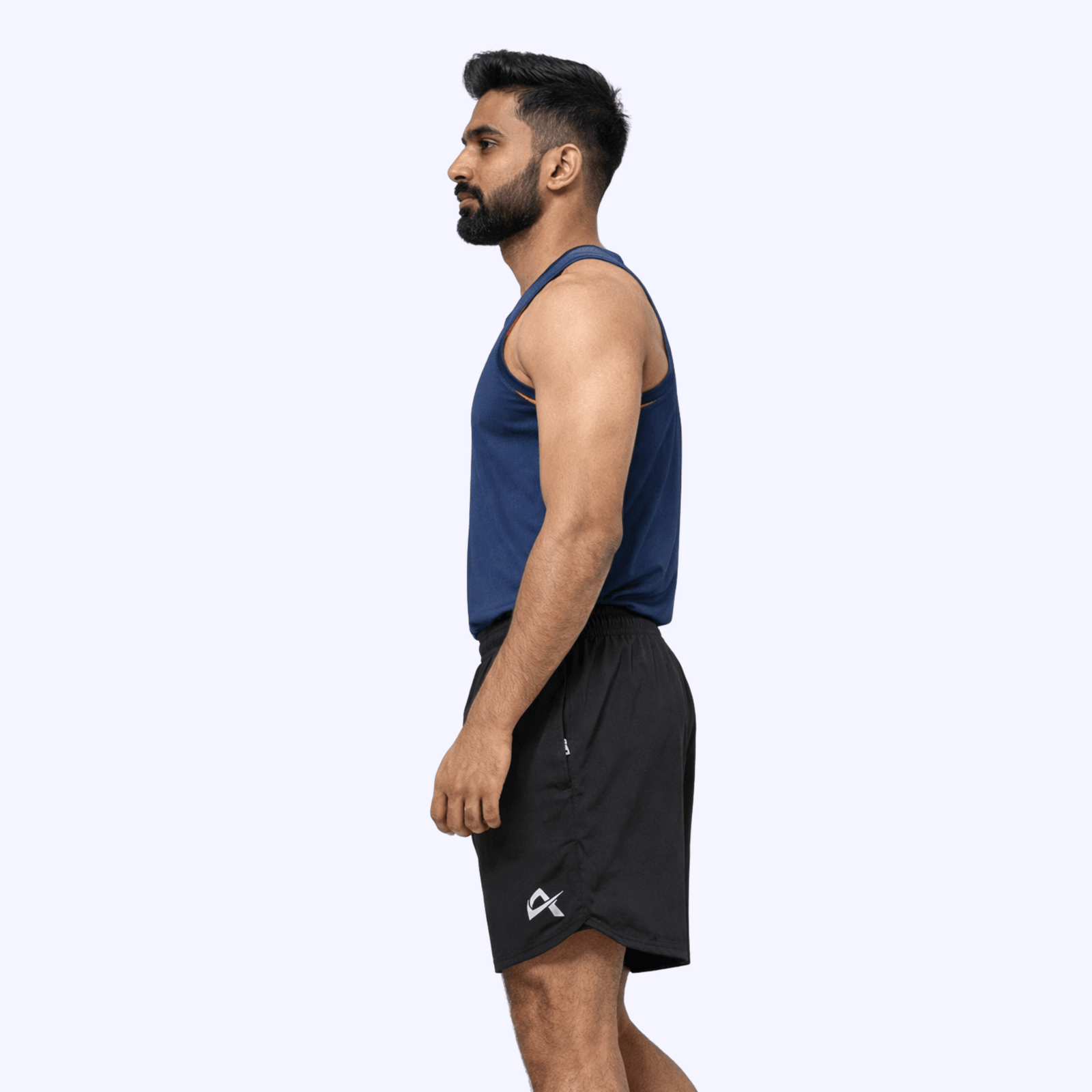 Side pose of a man wearing a blue tank top and black running shorts, exuding a sporty and stylish vibe.